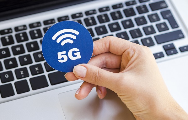 Henkilö pitelee 5G-merkkiä kannettavan tietokoneen edessä