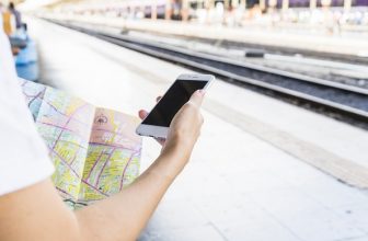 Henkilö käyttää älypuhelinta kartan kanssa junaraiteiden lähellä
