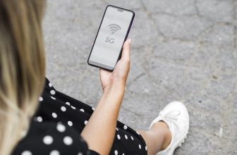 Nainen käyttää älypuhelinta, jonka näytössä näkyvät 5G- ja verkkosignaalin kuvakkeet