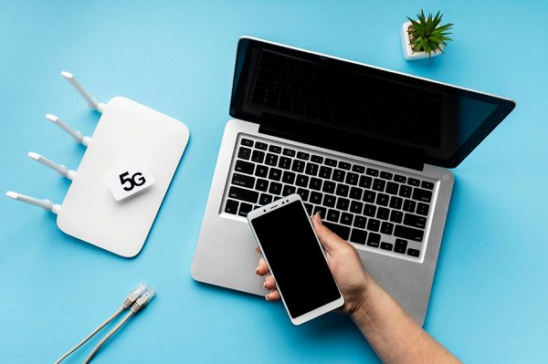 5G-reititin, kannettava tietokone ja älypuhelin pöydällä