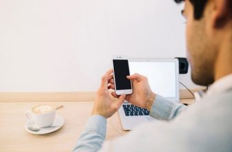 Henkilö tarkastelee älypuhelinta työpöydän ääressä